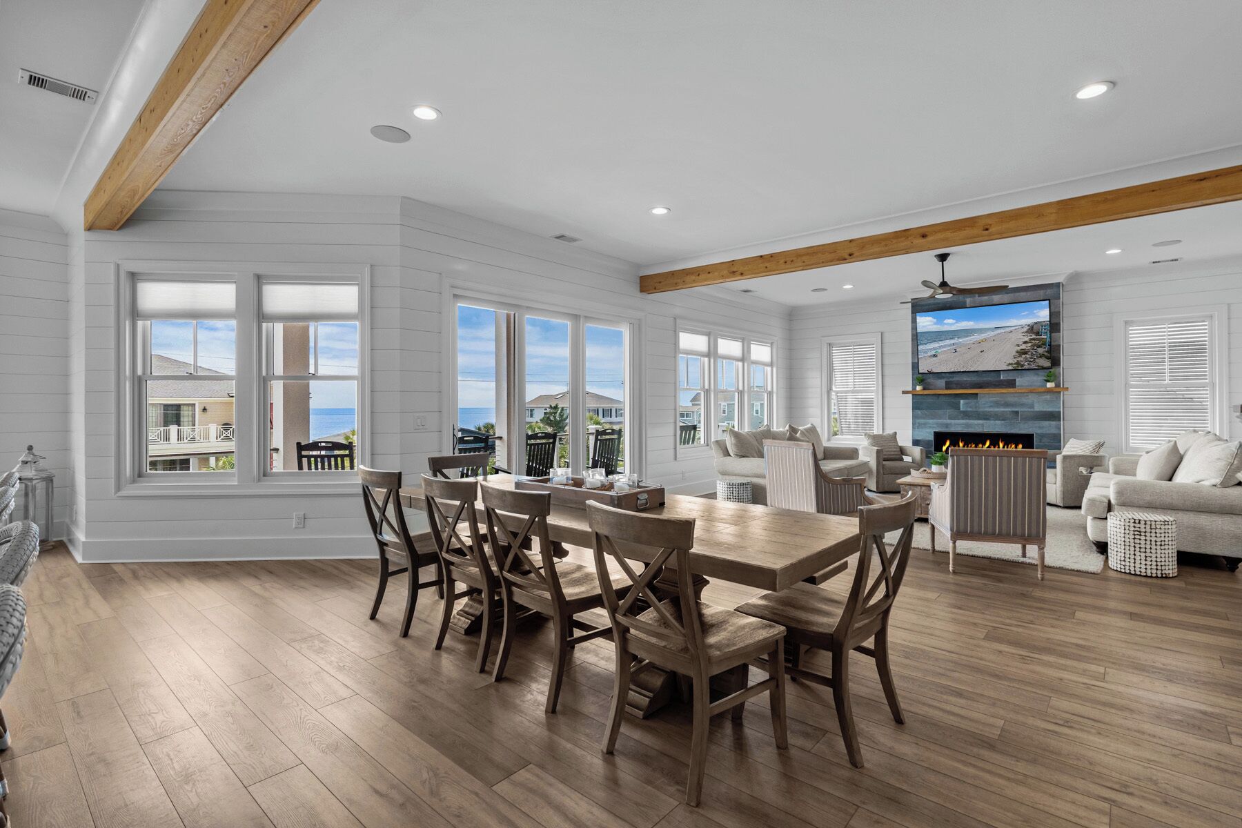 A spacious living room with a large wooden dining table and chairs, a fireplace, and a television mounted on the wall.