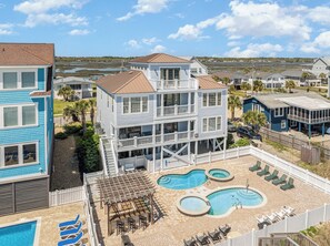 A multi-story building with a pool area, including a hot tub and lounge chairs. - Footprints On The Sand: Private Beach, Pools & Tiki Bar (Murrells Inlet)