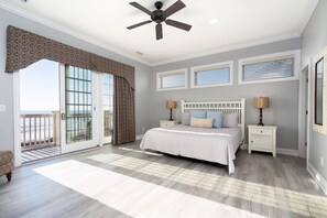 A bedroom with a large bed, a ceiling fan, a nightstand, and a view of the ocean through a sliding glass door. - Footprints On The Sand: Private Beach, Pools & Tiki Bar (Murrells Inlet)