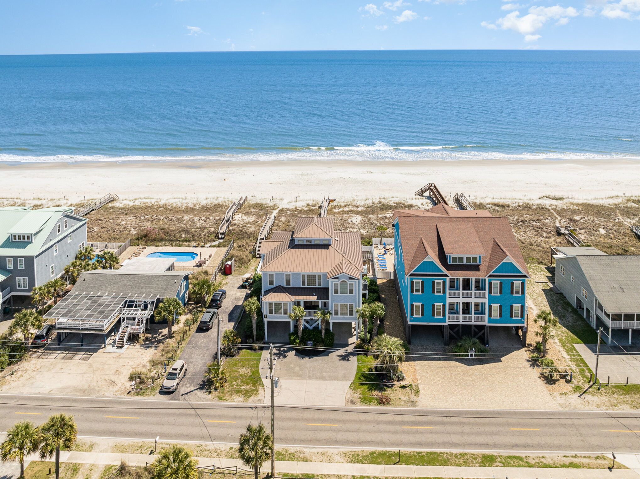 A beachfront property with multiple buildings, including a large blue house with a balcony, a swimming pool, and a beach access area.