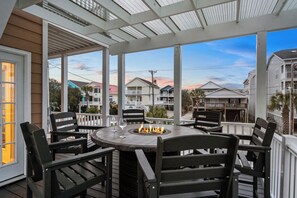 A covered outdoor seating area with a fire pit, surrounded by wooden chairs and a table.
