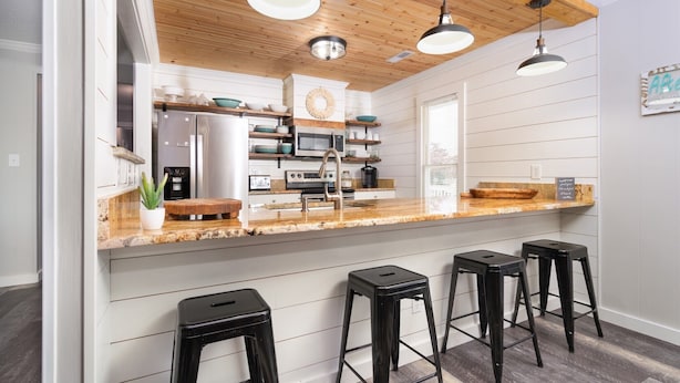 A modern kitchen with wooden ceiling beams, white cabinetry, a central island with bar stools, and a breakfast bar. - AfterMath: Walkable Garden City Beach Rental w/ Pool & Deck (Murrells Inlet)