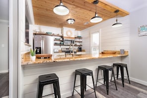 A modern kitchen with wooden ceiling beams, white cabinetry, a central island with bar stools, and a breakfast bar.