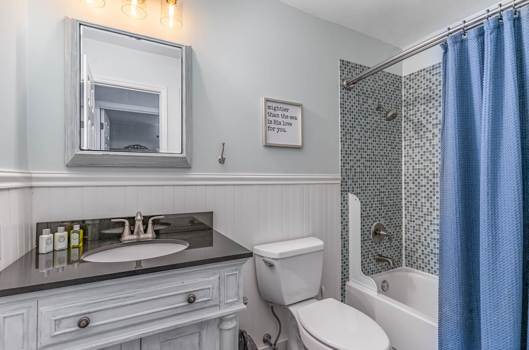 A bathroom with a white vanity, a sink, a toilet, and a shower with a blue curtain.