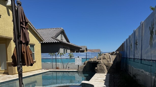 En swimmingpool med et boblebad, omgivet af en terrasse med stengulv og et lille græsstykke.