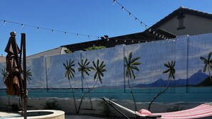 En baghave med kunstgræs, en hængekøje, en swimmingpool og et vægmaleri af palmer og bjerge.