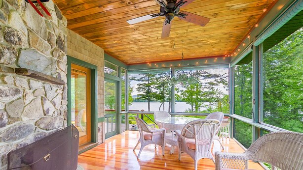 A covered patio with wicker furniture, a stone wall, and a view of a lake. - Waterfront Home -  Mid Coast Maine near Camden and Belfast (Belmont)