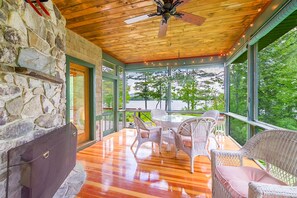 Un patio techado con muebles de mimbre, un muro de piedra y vista a un lago.
