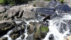 A rocky stream with a waterfall, surrounded by greenery and buildings in the background. - Waterfront Home -  Mid Coast Maine near Camden and Belfast (Belmont)