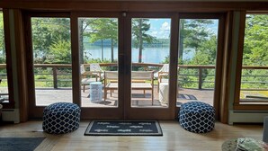 A room with a large sliding glass door leading to an outdoor deck with wooden furniture and a view of a lake. - Waterfront Home -  Mid Coast Maine near Camden and Belfast (Belmont)