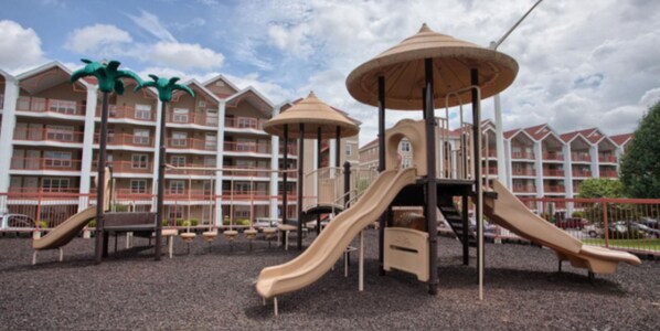 A playground with slides and swings, surrounded by a building with balconies.