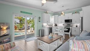 A modern kitchen with white cabinets, a dining area with striped sofas, and a view of a pool through glass doors. - Key Lime Cottage by Beach Boutique Rentals (Holmes Beach)
