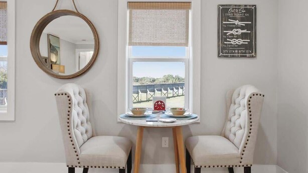 A room with two upholstered chairs, a round mirror, a window with a view, and a framed sign on the wall. - The Blue Heron Hideaway (Tybee Island)