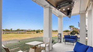 A covered outdoor patio with a table and chairs, a blue sofa, and a view of a golf course. - The Blue Heron Hideaway (Tybee Island)