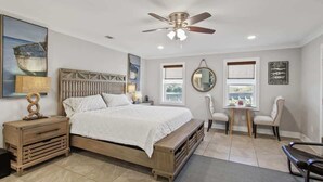 A bedroom with a bed, bedside tables, a ceiling fan, a window, and a chair. - The Blue Heron Hideaway (Tybee Island)