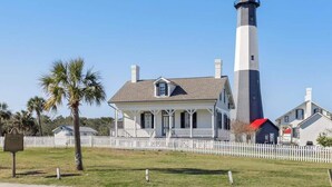 A lighthouse with a white and black exterior, a white picket fence, and a house with a porch in front. - The Blue Heron Hideaway (Tybee Island)