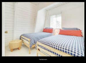 Una habitación infantil con dos camas, ropa de cama de cuadros y un taburete pequeño y redondo.