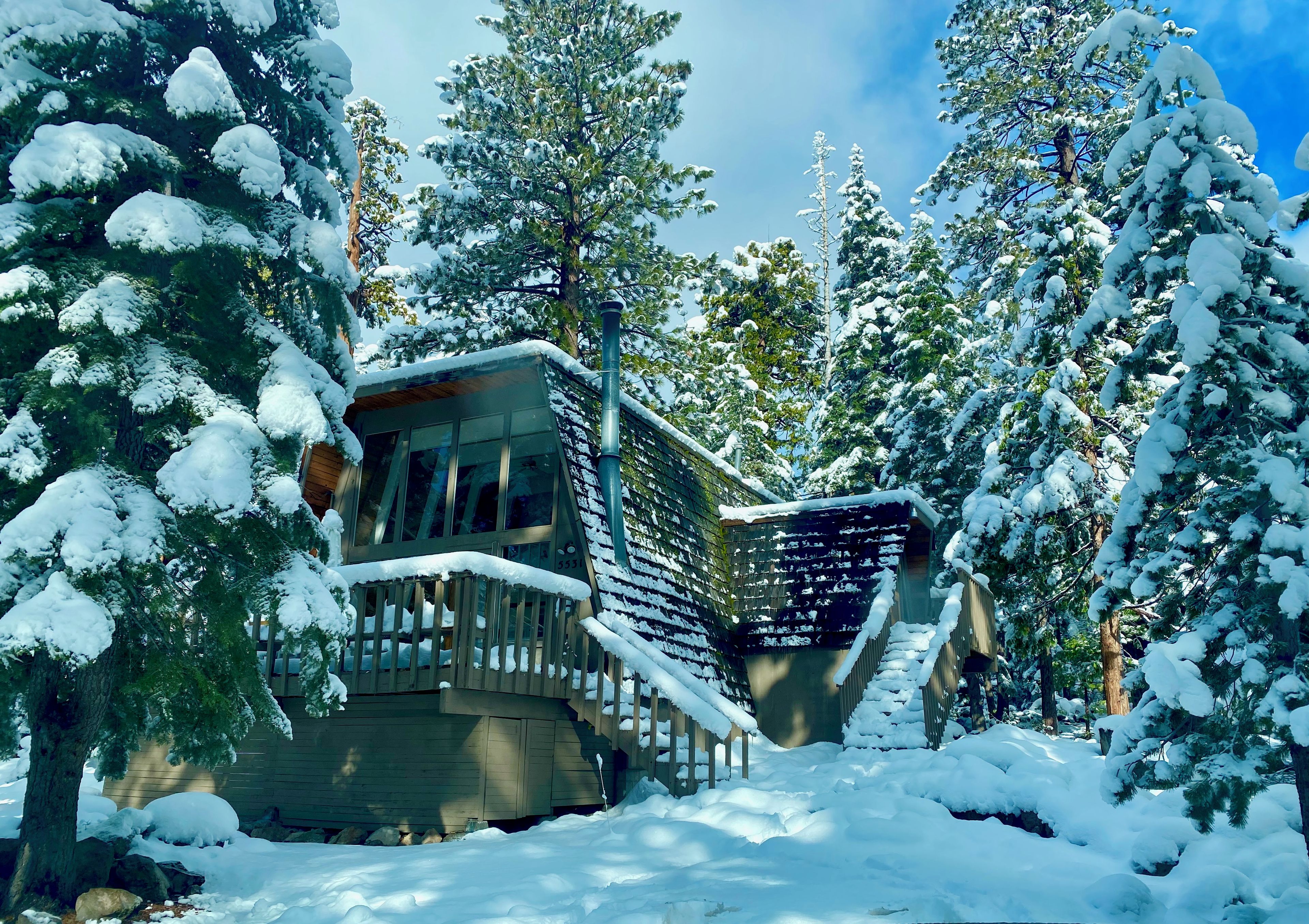 A cabin with a wooden deck and a glass door, surrounded by snow-covered trees.