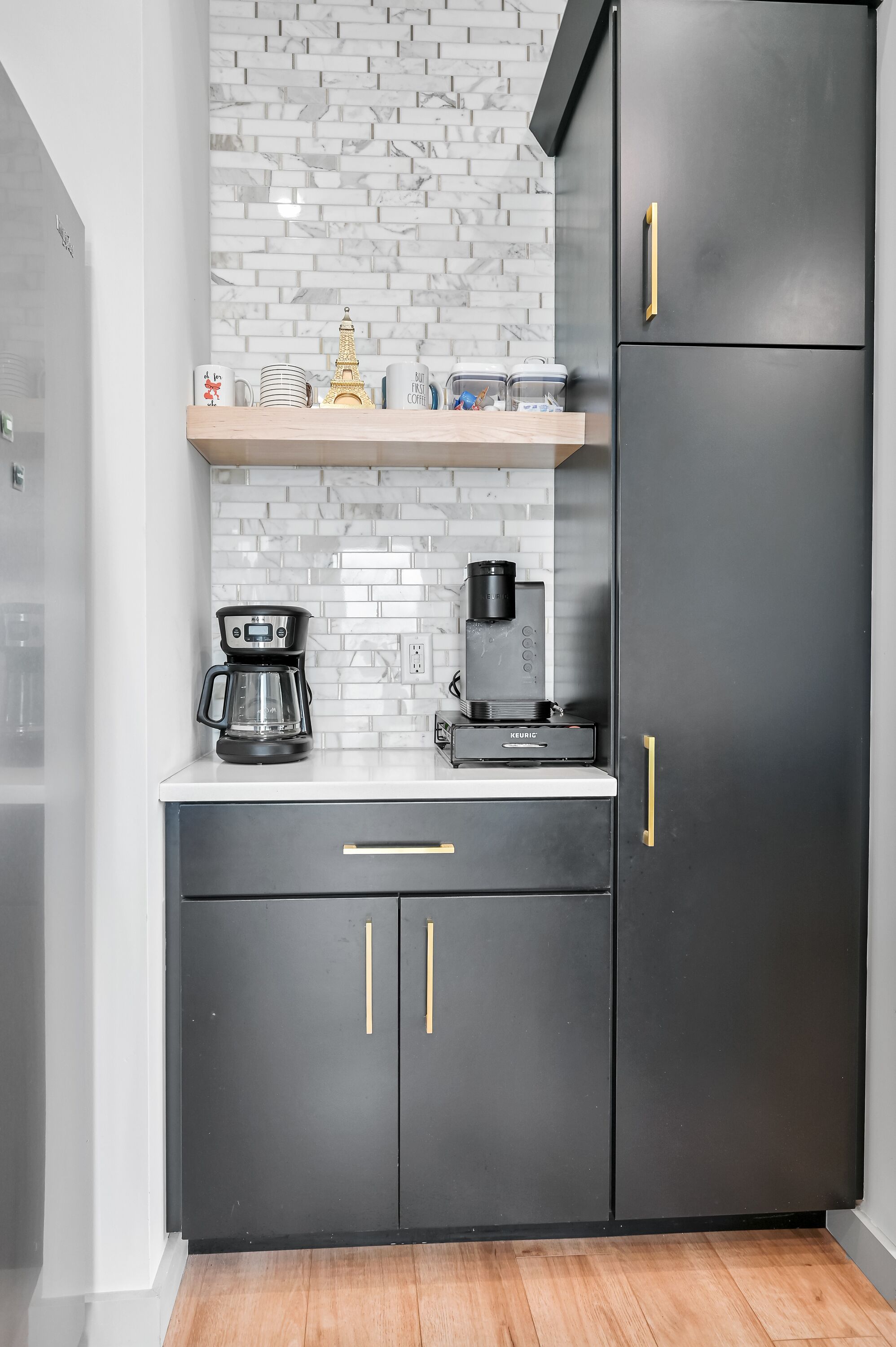 A modern kitchen with black cabinets, a white countertop, and a coffee maker.