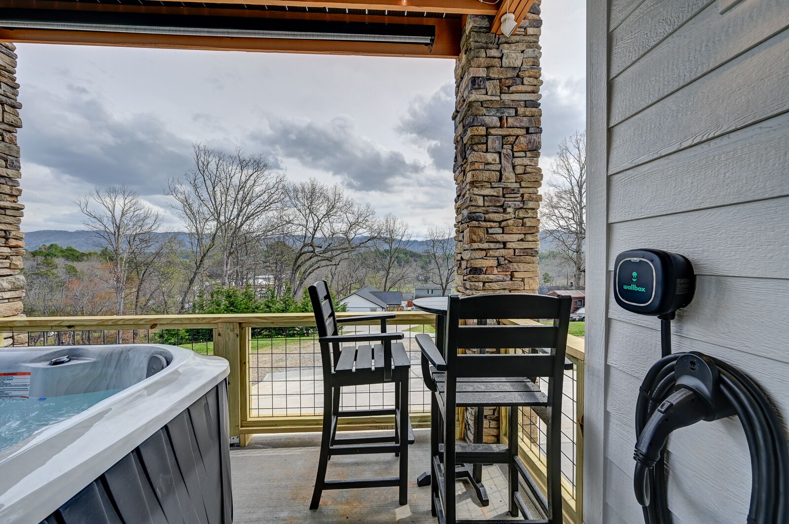 A covered outdoor area with a hot tub, two chairs, and a wall-mounted charging station.