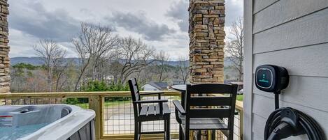 A covered outdoor area with a hot tub, two chairs, and a wall-mounted charging station.