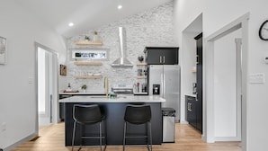 Een moderne keuken met een witte baksteen achterwand, roestvrijstalen apparatuur en zwarte barkrukken.