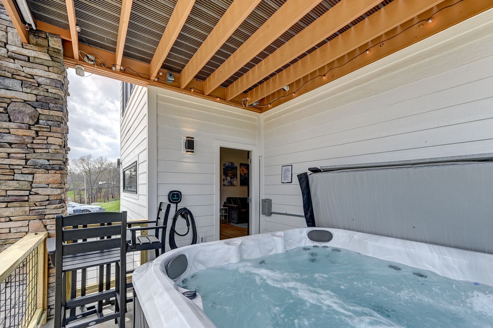 A hot tub under a wooden pergola with a stone wall and a bench.