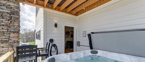A hot tub under a wooden pergola with a stone wall and a bench.