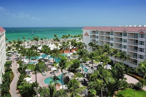Relax by the pool surrounded by palm trees and lounge chairs, with ocean views from the adjacent building's balconies.