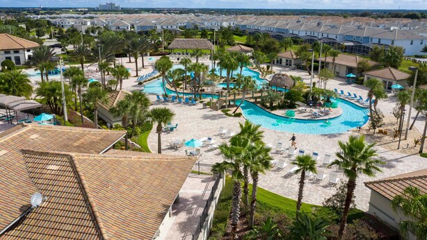 A resort with a central pool, palm trees, and a view of the surrounding buildings.
