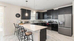 A modern kitchen with dark cabinetry, stainless steel appliances, a large island with bar stools, and a clock on the wall.