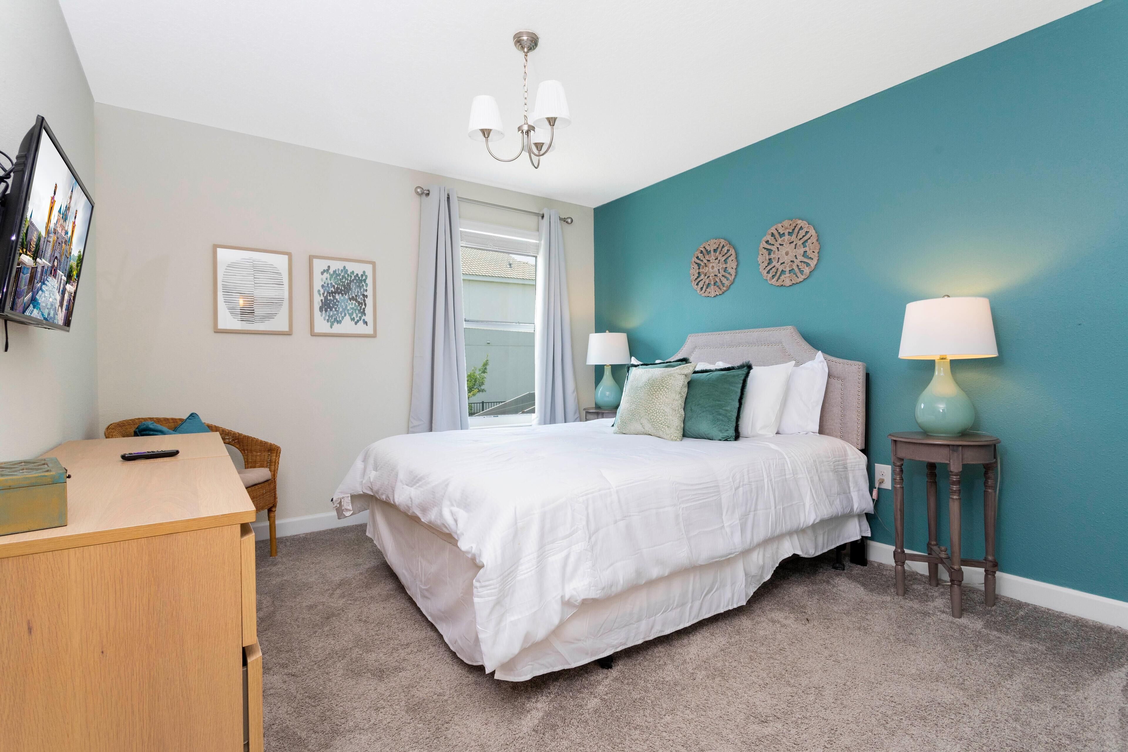 A bedroom with a bed, a desk, a chair, and a window.