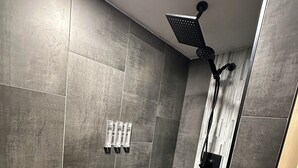A modern shower room with grey tiles, a black herringbone floor, and a ceiling-mounted showerhead.