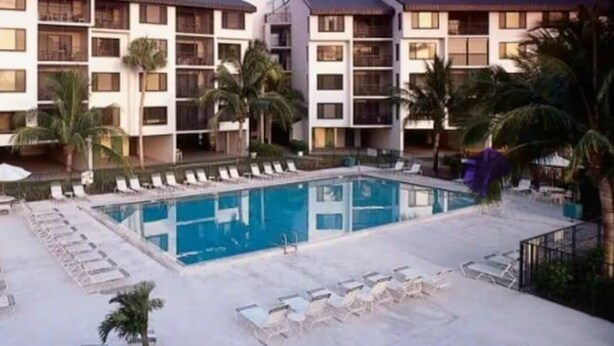A hotel with a swimming pool surrounded by lounge chairs and palm trees.