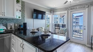 A modern kitchen with a black granite countertop, white cabinetry, and a flat-screen TV mounted above the island. - Seascape 1215 in Galveston (Galveston)