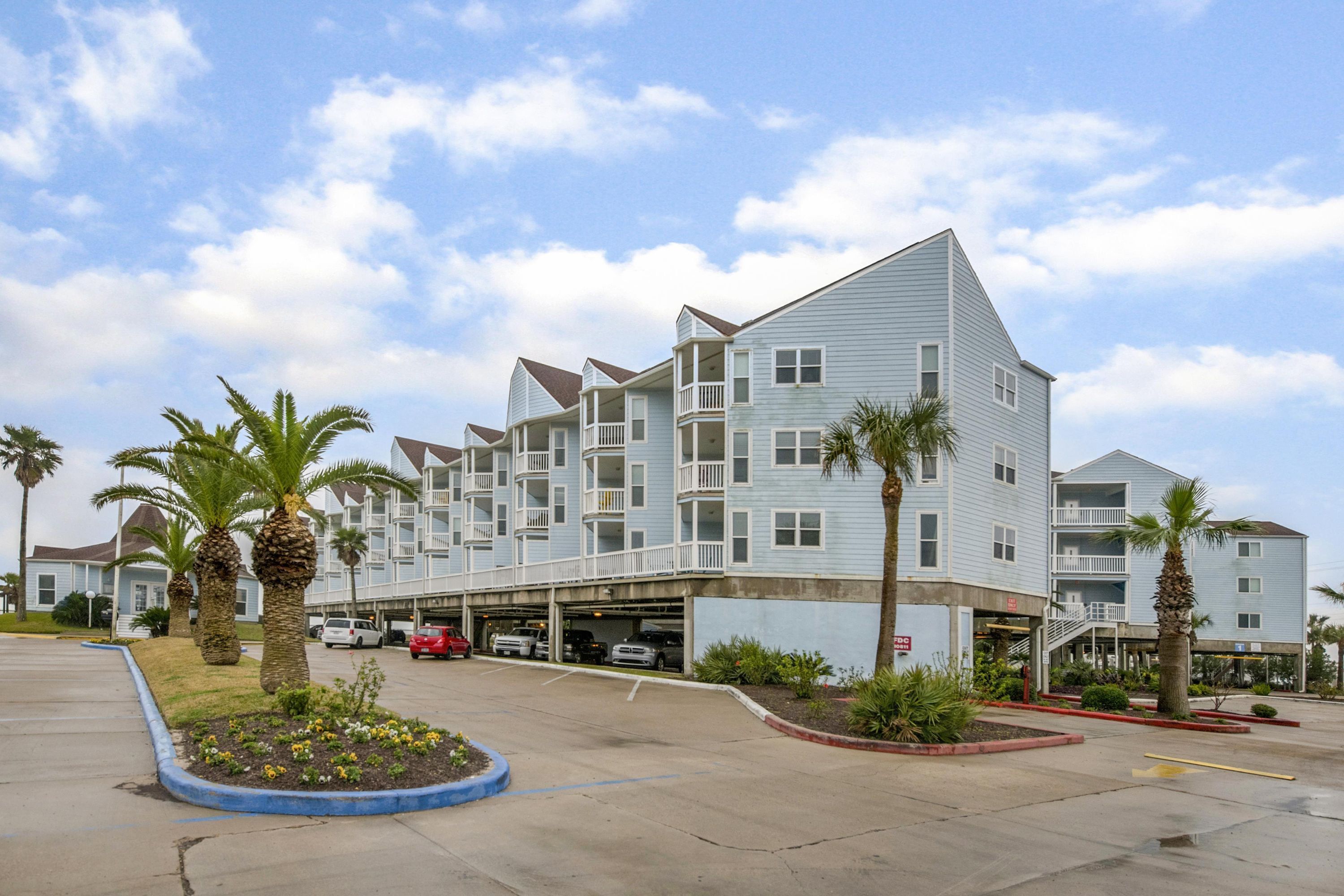 A multi-story hotel with a parking lot, palm trees, and a clear sky.