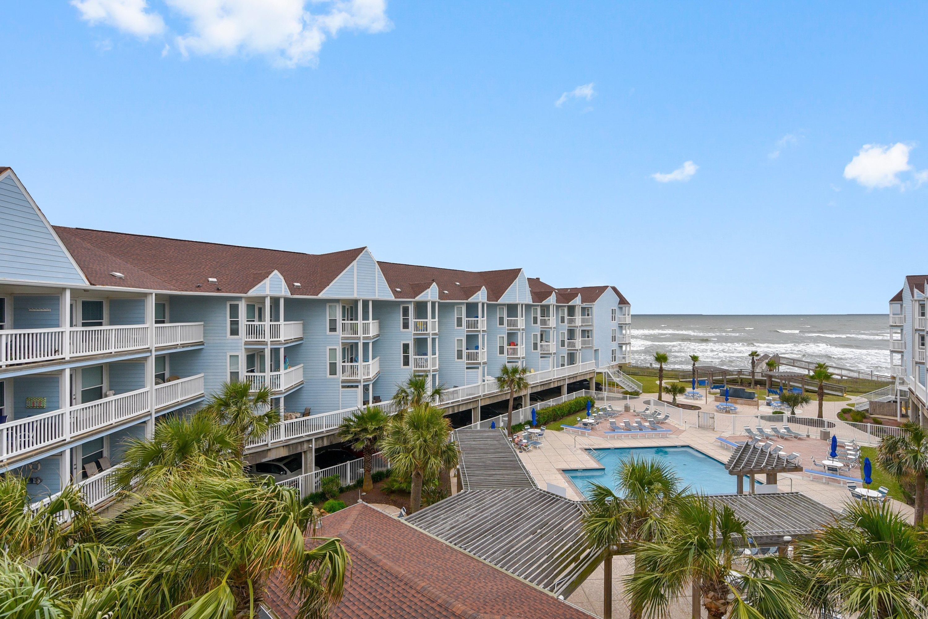 Een strandhotel met meerdere balkons, een zwembad en palmbomen.