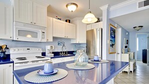 A kitchen with white cabinets, a stainless steel refrigerator, a microwave, and a stove. There are two blue placemats on the counter. - Seascape 1120 in Galveston (Galveston)