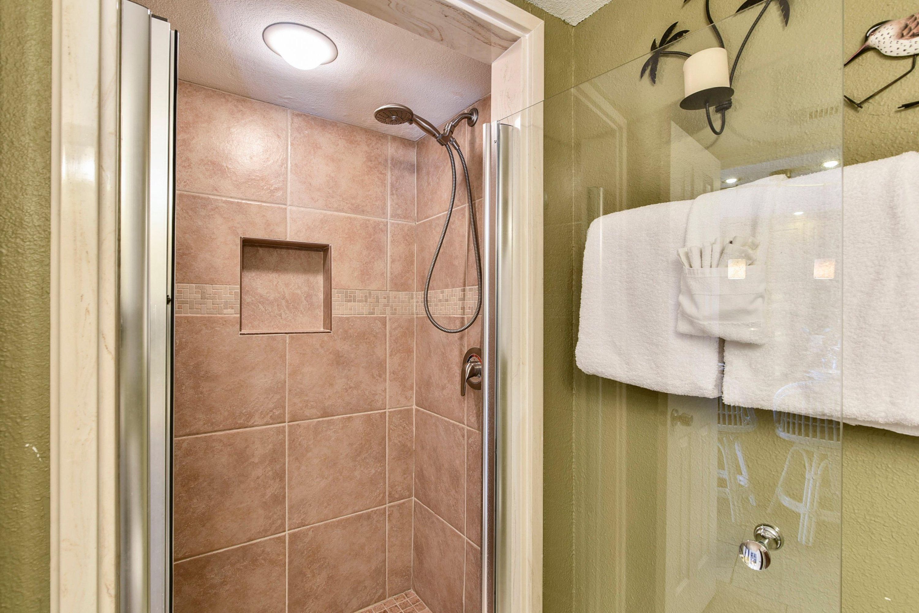 A glass-enclosed shower with a handheld showerhead and a wall-mounted faucet.