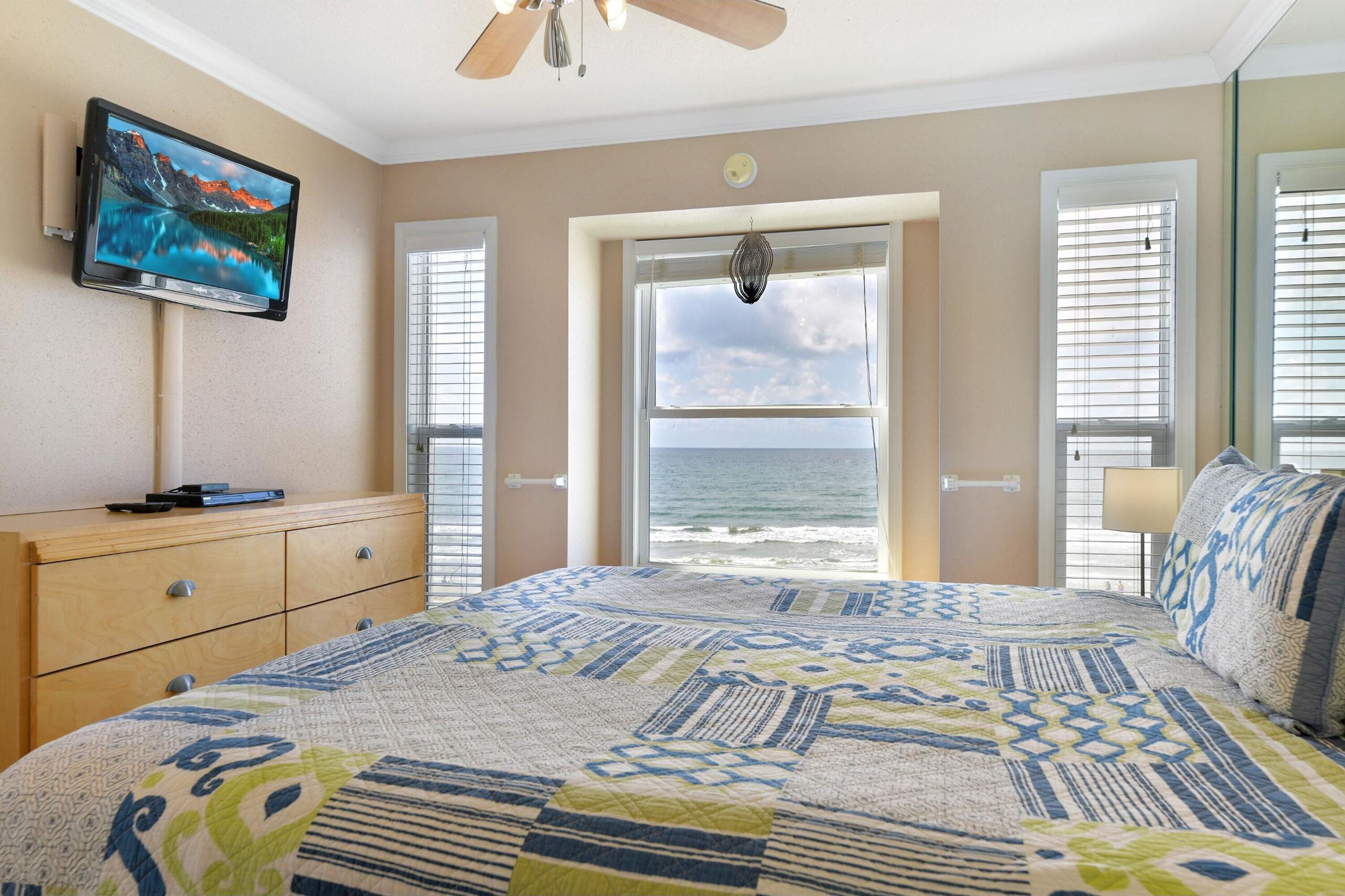 Een slaapkamer met een groot bed, een televisie aan de muur, een dressoir en uitzicht op de oceaan door een raam.