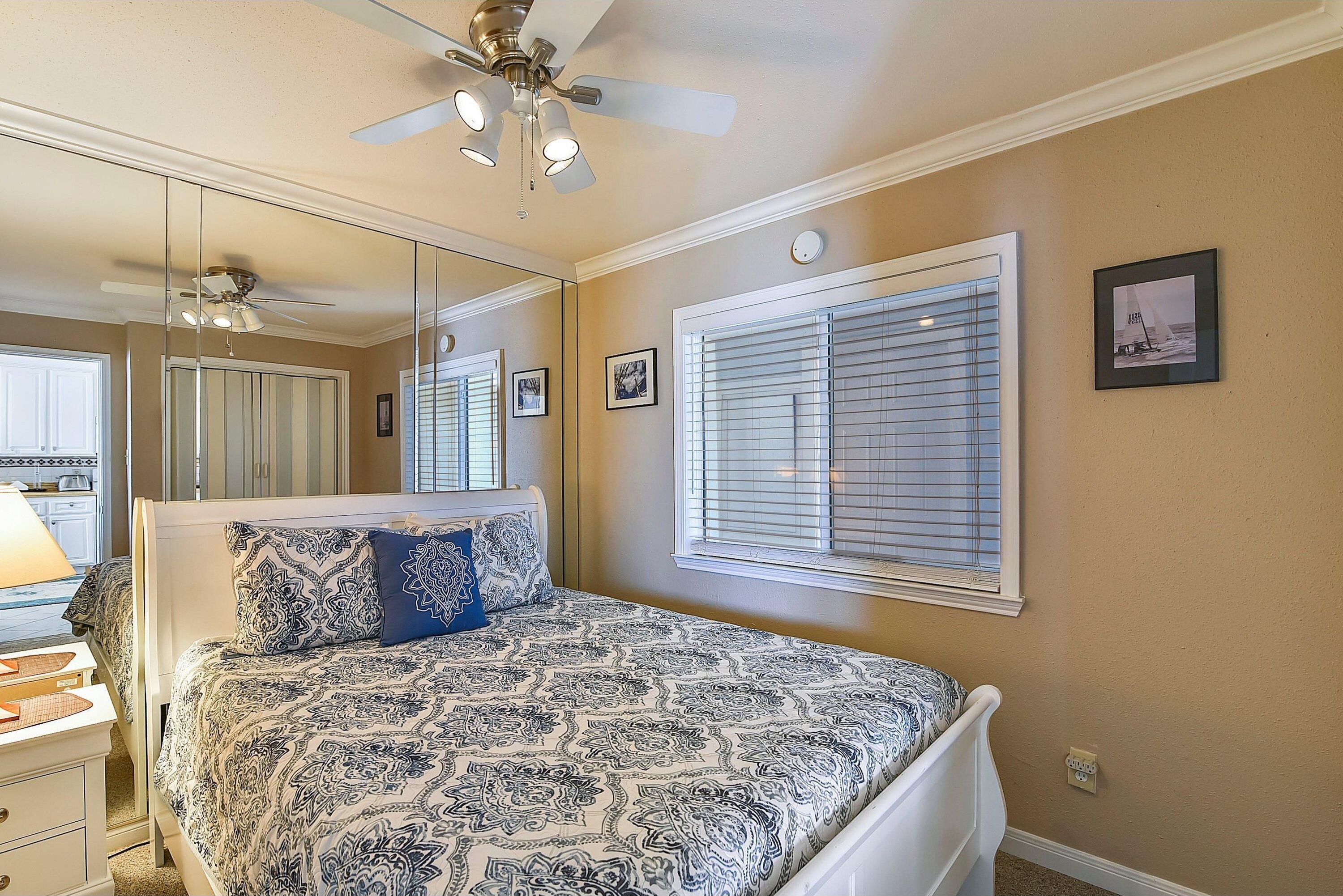 A bedroom with a bed, a ceiling fan, a window with blinds, and a mirror.