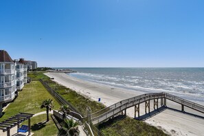 A beachside hotel with a boardwalk leading to the ocean, a grassy area, and a clear view of the sea.
