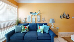 A blue sofa with colorful pillows, a wall with nautical decorations, and a lamp on a side table. - Seascape 1216 in Galveston (Galveston)