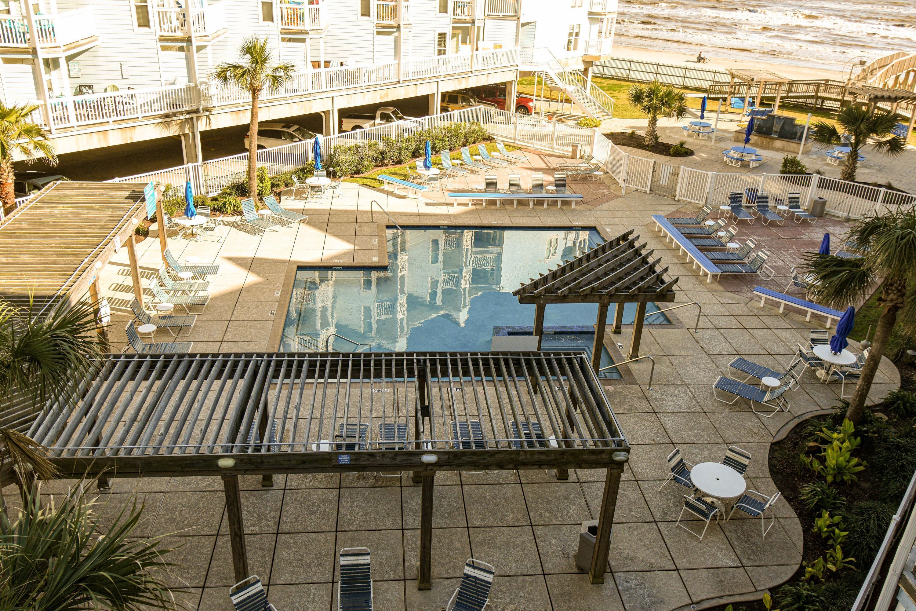 A rooftop pool area with lounge chairs and umbrellas, surrounded by a wooden deck and a covered seating area.