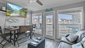 A living room with a TV, a wooden table, a bench, a couch, and a view of a deck. - Seascape 1318 in Galveston (Galveston)