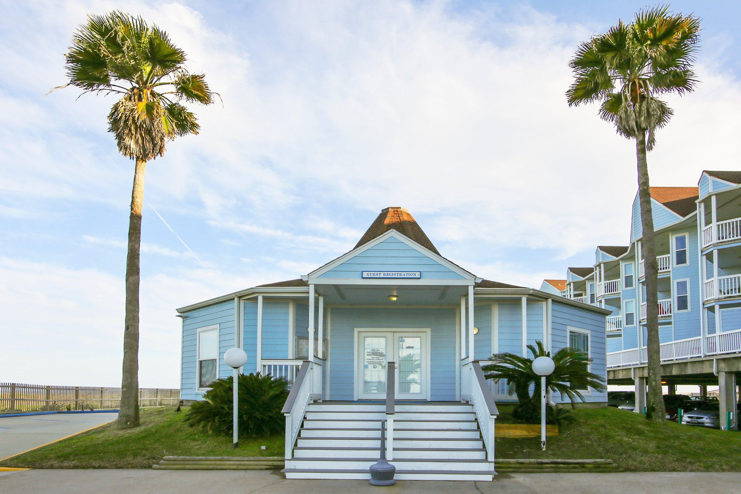 A guest registration building with a sign, steps, and palm trees.