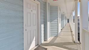 A corridor with a white door, a red EXIT sign, and a long hallway with windows and railings. - Seascape 1318 in Galveston (Galveston)
