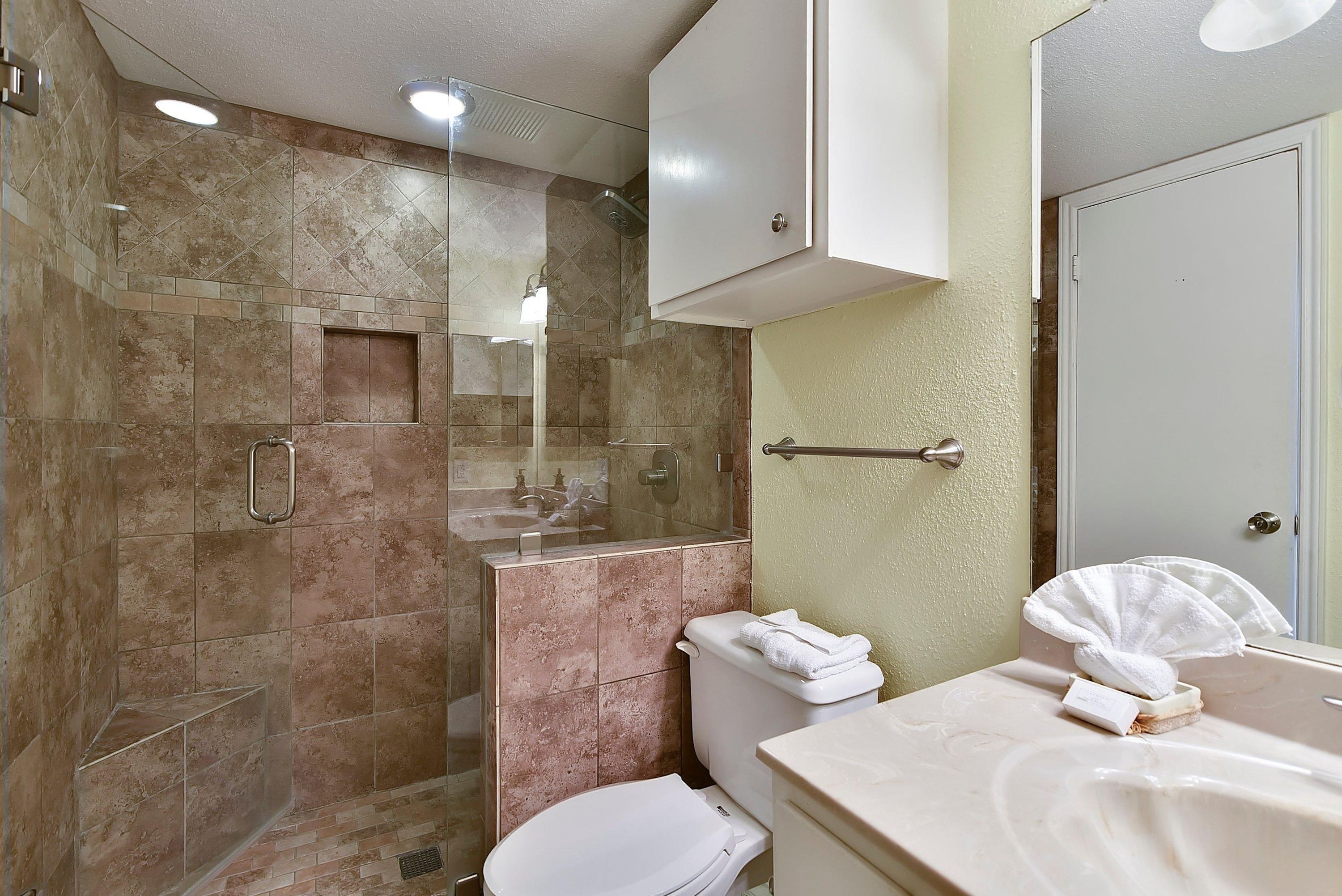 A modern bathroom with a glass-enclosed shower, a toilet, and a sink with a towel and soap.