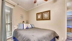 Un dormitorio con una cama, un ventilador de techo, una ventana con persianas y un cuadro colgado en la pared.