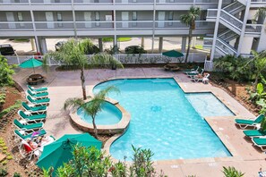 A hotel pool area with multiple lounge chairs and umbrellas, surrounded by a white fence and palm trees. - Casa Del Mar C279 in Galveston (Galveston)